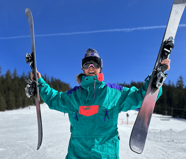 Skier in retro outfit holding up a pair of skis.